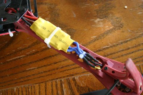 A picture of a yellow ESC zip-tied to the red arm of a quadcopter